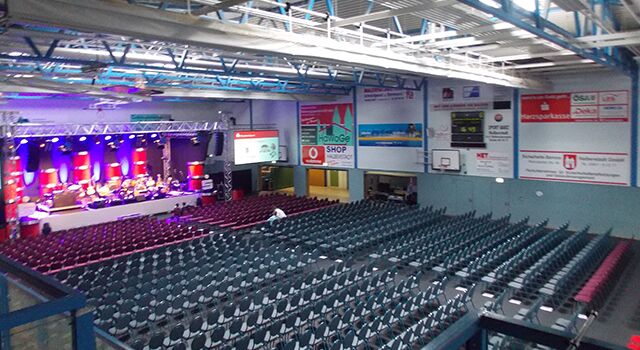 Leere Halle mit Bühne und vielen Stuhlreihen, bereit für Events.