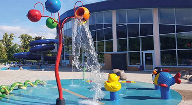 Spielplatz mit Wasserspielen und bunter Rutsche im Freien.