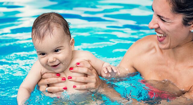 Lachende Frau hält lächelndes Baby im Schwimmbad.