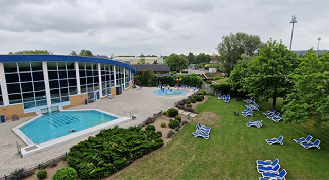 Außenbecken am Schwimmbad mit Liegestühlen und Bäumen an einem bewölkten Tag.
