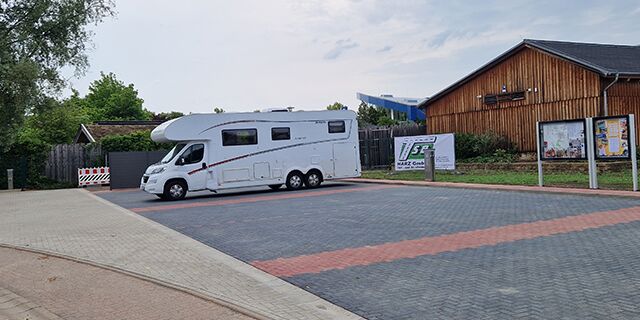 Wohnmobil steht auf einem leeren Wohnmombilstellplatz neben einem Holzgebäude.
