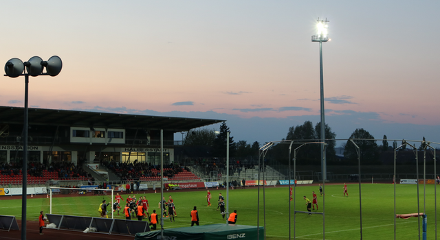Fußballspiel im Stadion bei Sonnenuntergang mit Flutlicht.