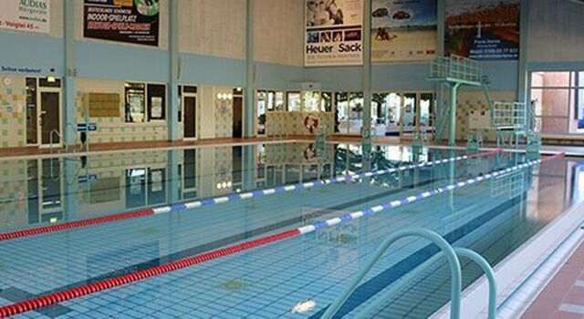 Leeres Hallenbad mit Startblöcken und Schwimmbahnen.