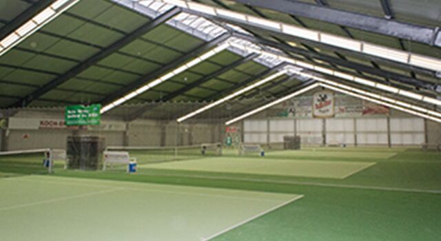 Innenansicht einer leeren Tennishalle mit mehreren Plätzen.