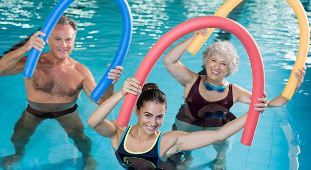 Drei Menschen machen Wassergymnastik mit Poolnudeln im Schwimmbad.