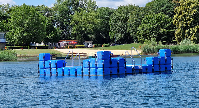 Ein schwimmende Ponton-Badeinsel auf einem See vor einem Strand.