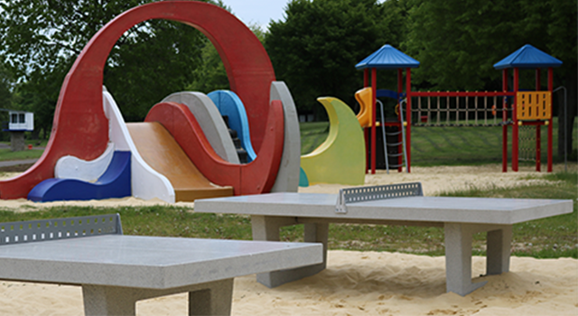 Spielplatz mit farbigen Rutschen und Tischtennisplatten im Sand.