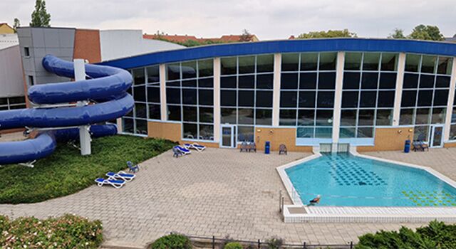 Schwimmbad mit blauer Rutsche und Liegestühlen außen.