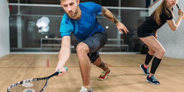 Zwei Personen spielen Squash auf einem Indoor-Platz.