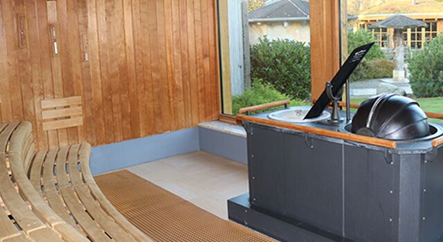 Innenansicht einer Sauna mit Holzbänken, Aufgussofen und Ausblick in den Saunagarten.