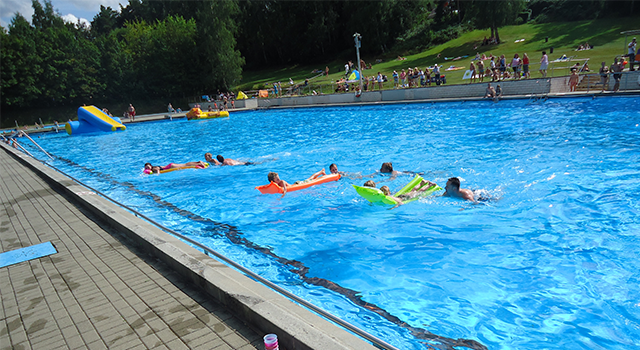 Menschen schwimmen auf Luftmatratzen in einem Freibad.